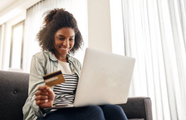 İnternetten daha iyi bir fiyat alacağımı biliyorum. Bilgisayarını kullanırken kredi kartını tutan genç bir kadın.