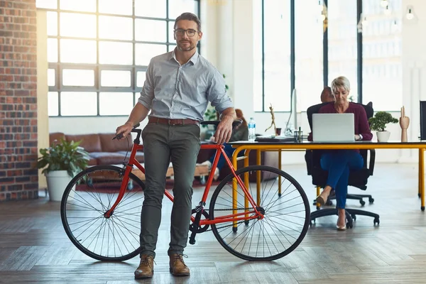 We prefer keeping a casual office setting. Portrait of a mature designer standing in an office with his bicycle