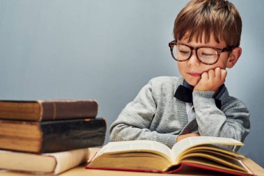 Büyümek bilginin sonucudur. Küçük zeki bir çocuğun gri bir arka planda kitap okurken çekilmiş bir fotoğrafı.
