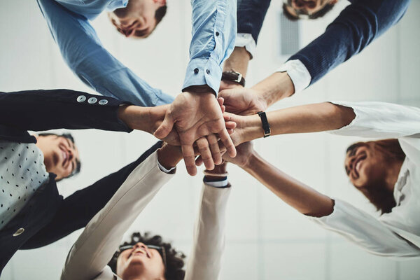 Here we go guys. Low angle shot of a group of businesspeople forming a huddle with their hands inside of the office during the day