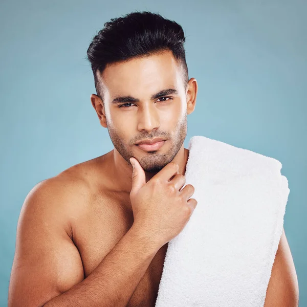 Skincare, health and face of model from India posing for health, wellness and dermatology after cleaning, facial or shaving against blue background. Portrait of beauty man with towel for self care.