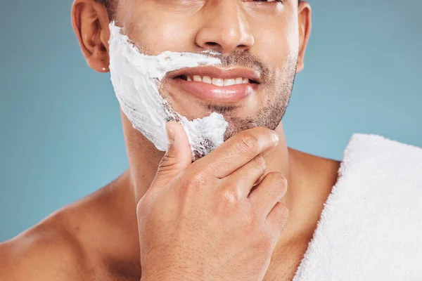 Man with shaving cream on face, beard maintenance and skincare for mens health and beauty treatment with blue background. Health, skin care and facial hair, morning shave bathroom routine with towel