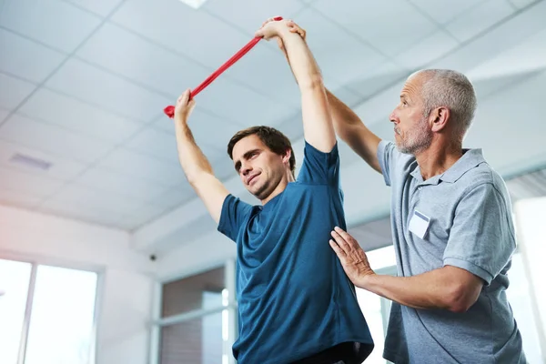 Theres no reason to make your injuries an impediment. Low angle shot of a handsome mature male physiotherapist helping a patient stretch with resistance bands