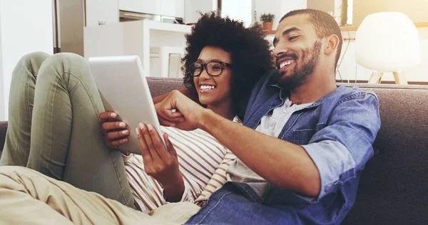 stock image Browsing the internet together. a cheerful young couple seated on a couch while browsing on a digital tablet together in the living room