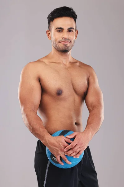 Fitness, portrait and man with a medicine ball for sports, workout and exercise against a grey studio background. Wellness, training and portrait of a young Arab athlete happy with body cardio.