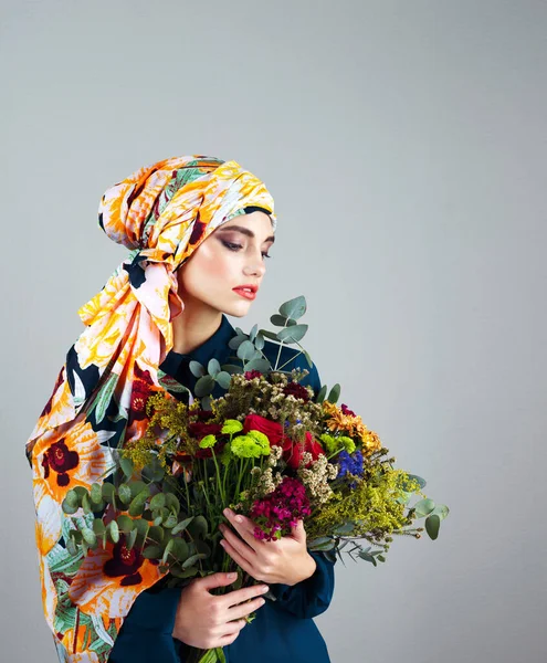 他们给你的世界带来了色彩 一个自信的年轻女子头戴五颜六色的头巾 拿着一束灰色背景的花的摄影棚照片 — 图库照片