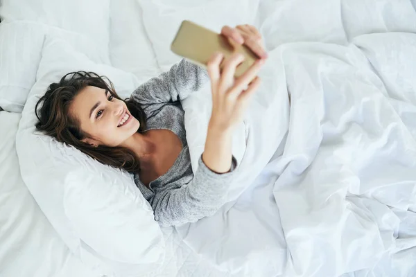 是时候更新我的社交媒体形象了 白天躺在床上用手机打字的年轻貌美的女人 — 图库照片