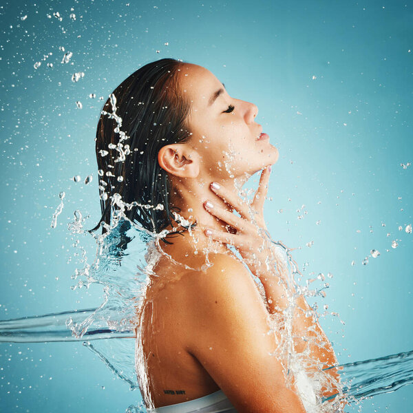 Water, hydration and cleansing with a woman in studio on a blue background with a liquid splash for hygiene. Relax, luxury and wellness with an attractive young female washing in a bathroom or shower.