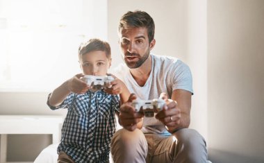 Benden daha iyi oluyorsun, evlat. Genç bir çocuk ve babası video oyunları oynuyorlar.