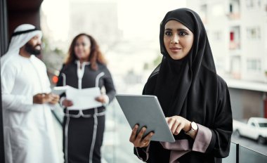 Balkonda iş var. İş yerinin balkonunda tablet kullanan geleneksel İslami kıyafetler giymiş çekici genç bir iş kadını.