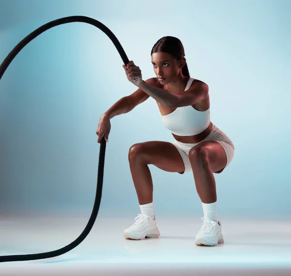 stock image Woman, battle rope and exercise on blue background in studio resistance training, energy sports or cardio workout. Personal trainer, fitness model or person with wellness health goals for arm muscles.