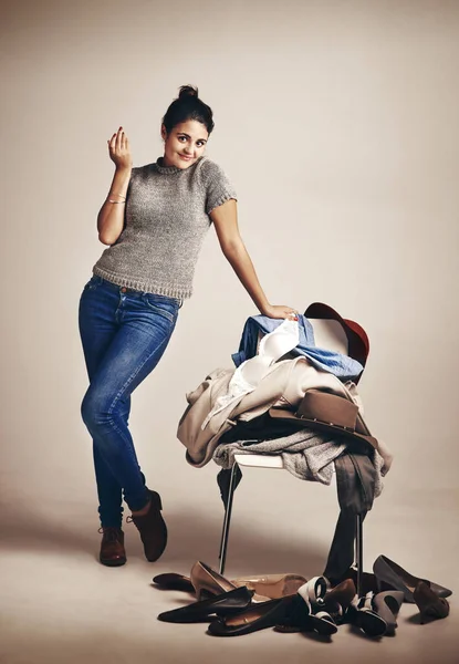 Stock image So many clothes, so little time. Studio shot of a young woman choosing clothing piled on a chair against a brown background