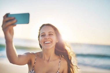 Mutluluğunu herkesle paylaş. Genç bir kadın sahilde selfie çekiyor.