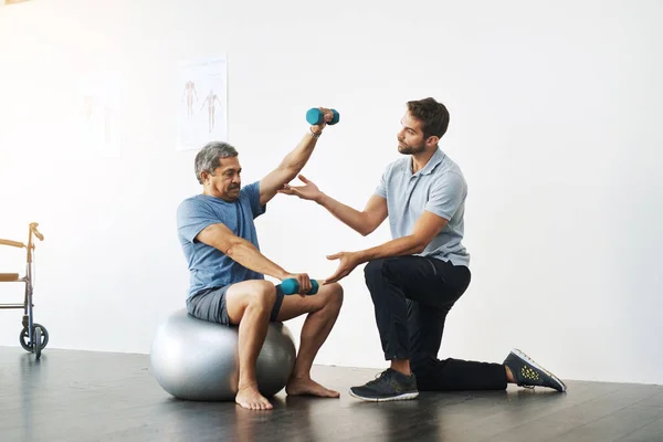 动作又慢又容易 在诊所帮助成年男性病人进行运动锻炼的年轻男性理疗师 — 图库照片