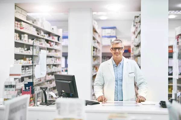 We have endless amounts of medication. Portrait of a cheerful mature male pharmacist standing behind the counter while looking at the camera in a pharmacy