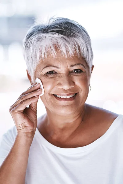 stock image She always goes for the natural look. Portrait of a cheerful mature woman applying makeup remover on her face while looking at the camera