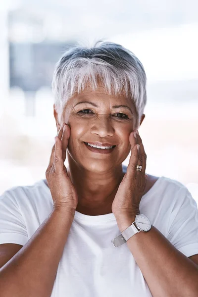 stock image She looks younger with age. Portrait of a cheerful mature woman applying makeup remover on her face while looking at the camera