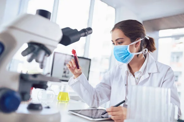 stock image I think Ill start with this vile. a focused young female scientist wearing a surgical mask and holding a vile of blood inside a laboratory