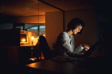 Gün bitmeden hallediyorum. İş yerinde gece geç saatlerde dijital tablet kullanan genç bir iş kadını.