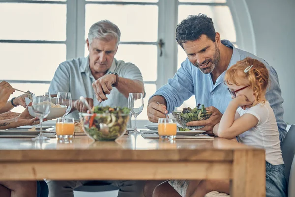 Dinner, family and child eating food at dining room table together at retirement home. Senior grandparent, happy father and young girl upset about conversation or dad teaching child healthy lifestyle.