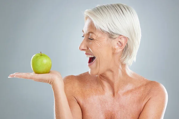 Beauty, apple and excitement with a senior woman in studio on a gray background to promote healthy eating. Food, fruit and diet with a mature female posing for nutrition vitamins or health lifestyle.