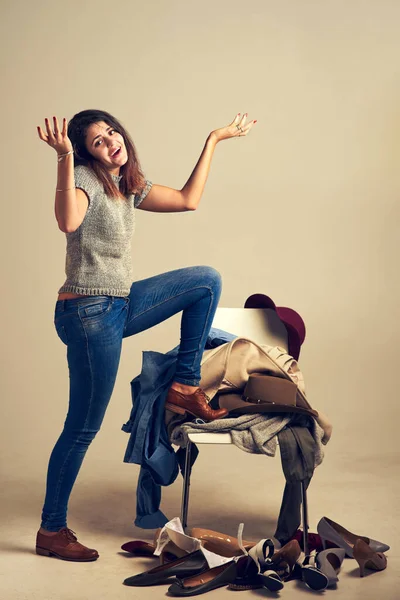 stock image All these clothes and still nothing to wear. Studio shot of a young woman choosing clothing piled on a chair against a brown background