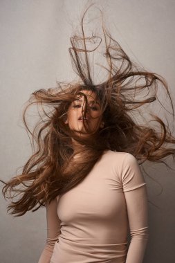 Dağınık saçlar, umurumda değil. Stüdyoda rüzgarla poz veren güzel bir genç kadının portresi.