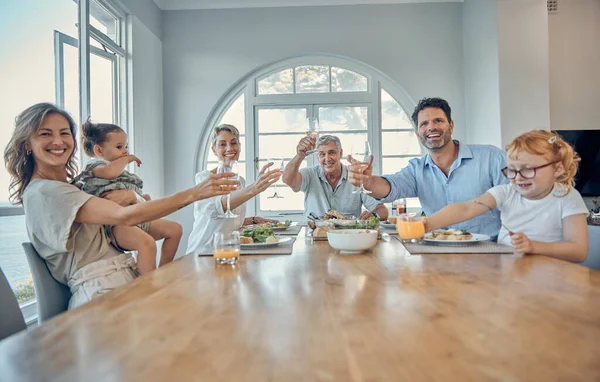 Family, dinner food and cheers of a mother, senior people and children happy at home. Portrait of a happy toast, mother and father with children care at a table eating at a house with happiness.
