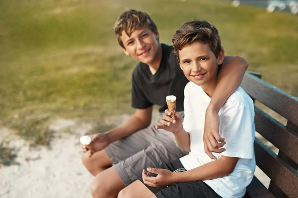 幸せは買えませんが アイスクリームを買うことができます ビーチのベンチに座っている間にアイスクリームコーンを食べている2人の幸せな兄弟の肖像画 — ストック写真