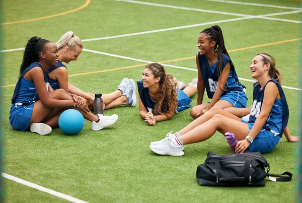 Sports, field and women team relax on grass with fitness gear talking about game, goal strategy and being social together. Happy, diversity and young girl netball group or people rest on sport pitch.
