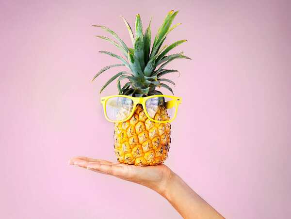 When life hands you pineapples make pina coladas. a woman holding a pineapple with glasses on against a pink background
