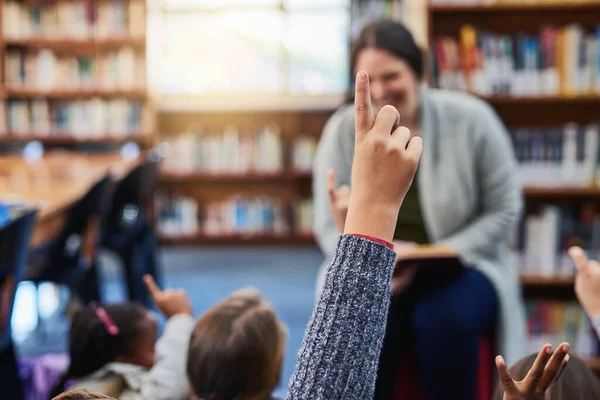 孩子们有许多问题 激发了他们好奇的头脑 一个小学生在图书馆向他的老师举手 — 图库照片