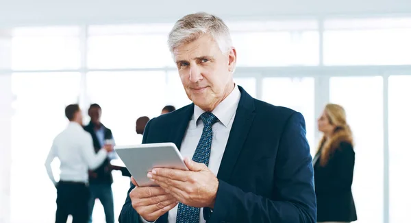 If only we had this back in my day. Cropped portrait of a handsome mature businessman using a tablet in the office with his colleagues in the background