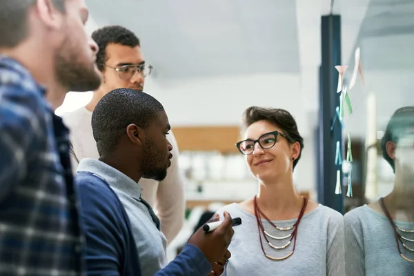 stock image Planning our work for the day. a group of designers brainstorming with notes on a glass wall in an office