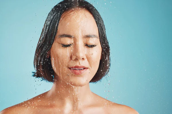 Shower, studio and woman cleaning her face and hair for wellness with blue background and mockup space. Beauty, water and wet young girl washing and grooming for healthy hygiene or relaxed self care.
