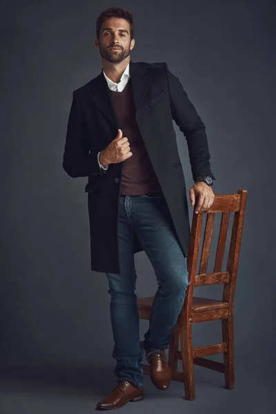 时尚的目标 一个穿着时尚的年轻人站在灰色背景的椅子旁边的工作室肖像 — 图库照片