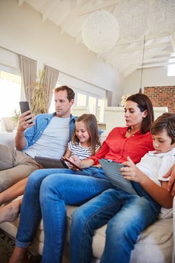 Aileden uzaklaştırılmış. Oturma odasındaki kanepede birlikte oturan genç bir aile çeşitli medya ve cihazlarla dikkatleri dağılıyor.