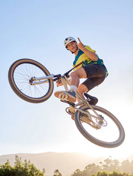 Bike, jump and rock on hand sign with a man bmx rider jumping over a ramp on a trail or course in nature. Sky, mountain and cycling with a male athlete jumping in mid air during fitness exercise.