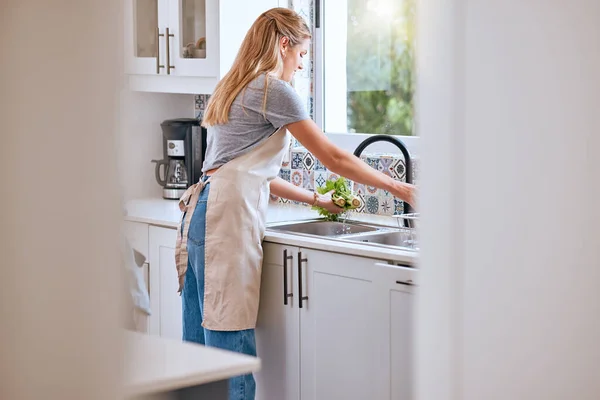 Woman, cooking and cleaning food or vegetable with water under kitchen tap for healthcare, wellness and safety home. Female chef or housewife with green lettuce for salad, lunch or dinner for diet.