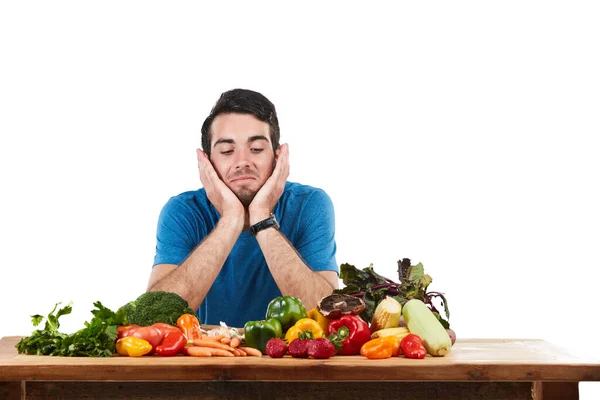 他对自己的新饮食不满意 演播室拍摄的是一个年轻男子与各种新鲜蔬菜在白色背景下摆姿势时看上去毫无兴趣的样子 — 图库照片