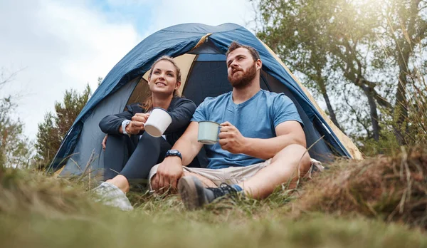 stock image Camping, tent and nature couple with coffee, tea or hot chocolate relax in outdoor forest or woods. Grass field trees, morning view and camper people bond, talk or enjoy quality time peace or freedom.