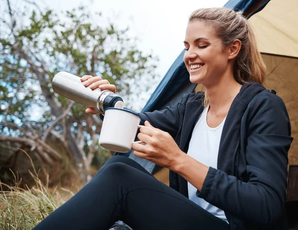 Camping, coffee and woman in nature by tent on vacation, holiday or trip. Tea, travel and female camper from Canada relaxing in woods, forest or grass field while pouring hot beverage from bottle