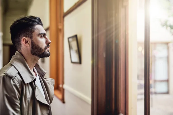stock image Taking in the day from his window. a handsome young man standing by a window looking deep in thought