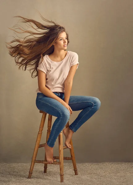 漂亮的头发把它们吹散了 摄影棚拍摄的是一个漂亮的年轻女子坐在一张平平的背景的凳子上 — 图库照片