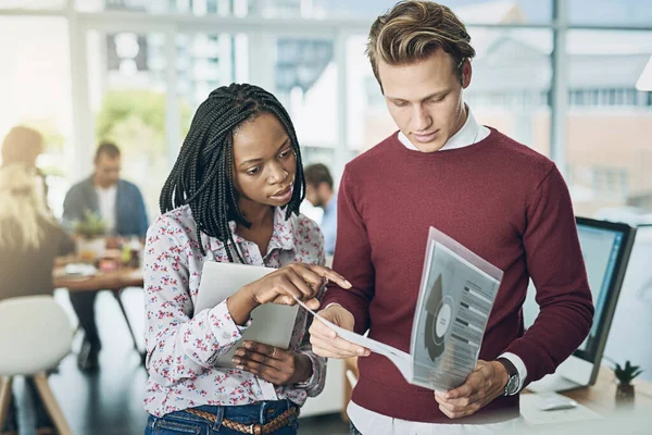 stock image Daily reporting gives them a strategic view on business. two young colleagues discussing paperwork together in a modern office