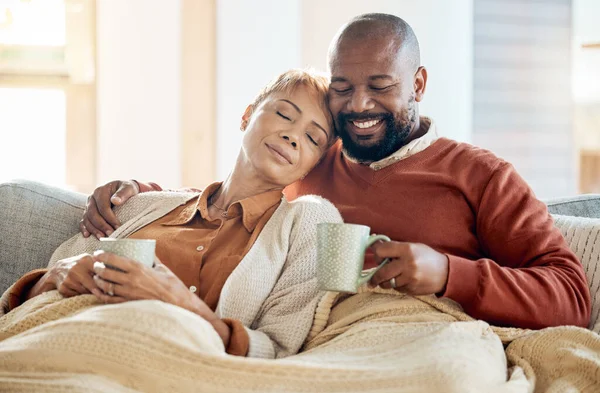 Black couple relax on sofa with coffee, blanket and smile on winter weekend morning in home. Peace, comfort and love, happy man and tired woman, cozy time on couch with drink in living room together