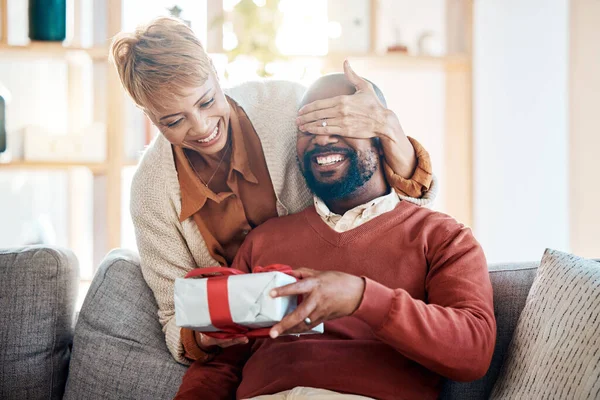 Black couple, surprise gift and Christmas present in festive summer season from wife with love, happiness and holiday celebration. Black woman, happy man and smile the living room home sofa together.