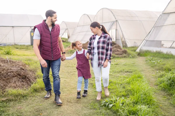Farming, family and sustainable lifestyle with child and parents walking together on a field for love, bonding and support in countryside. Happy girl, man and woman on an agro and agriculture farm.