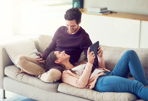 stock image Some relaxing a home with our mobile devices. a cheerful young couple relaxing on the sofa together while using their mobile devices at home