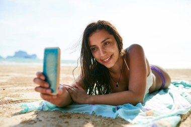 Plaj özçekimleri. Genç bir kadın sahilde yatarken selfie çekiyor.